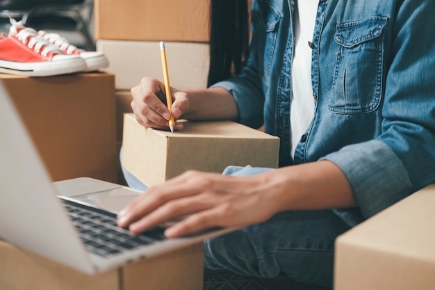 Closeup hand of young woman writing address on parcel box for delivery order to customer, shipping and logistic, merchant online and seller, business owner or sme, online shopping.