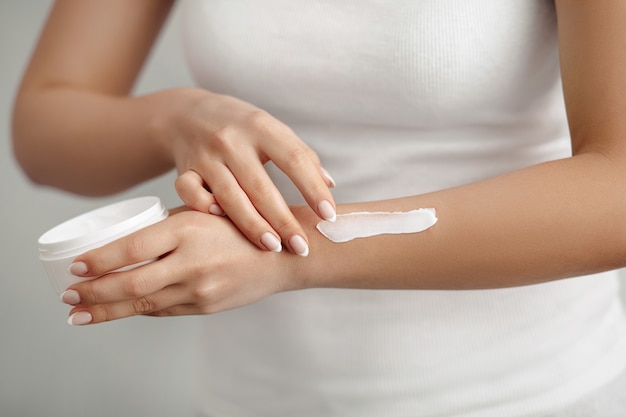 Closeup of hands applying moisturizer. Beauty woman holding a bottle of skin cream.