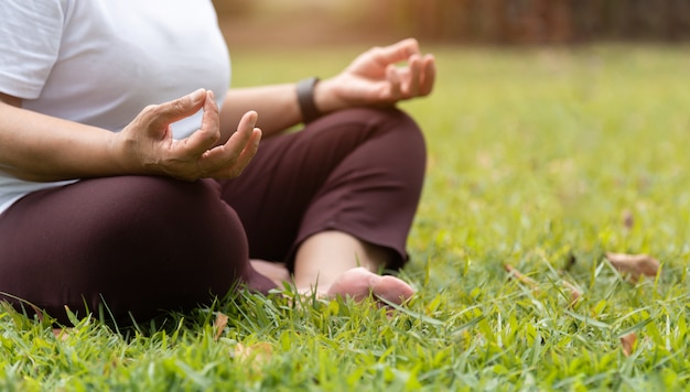 Closeup on hands. Asian Senior Woman in white shirt practicing Yoga at park.