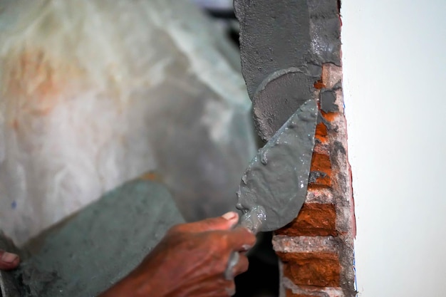 Closeup hands of builder holding mortar pan and plastering walls with cement in construction site