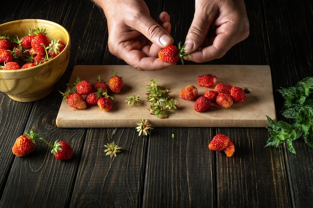 Closeup hands chef sorting through fresh strawberries on the cutting board of the restaurant kitchen