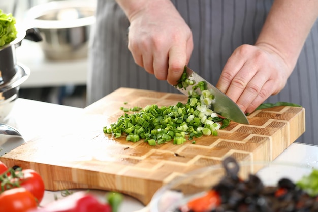 Closeup of hands of cook holding knife for cutting green onions