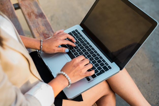 Closeup of the hands of a female executive working on her laptop sitting on a bench anywhere outdoors