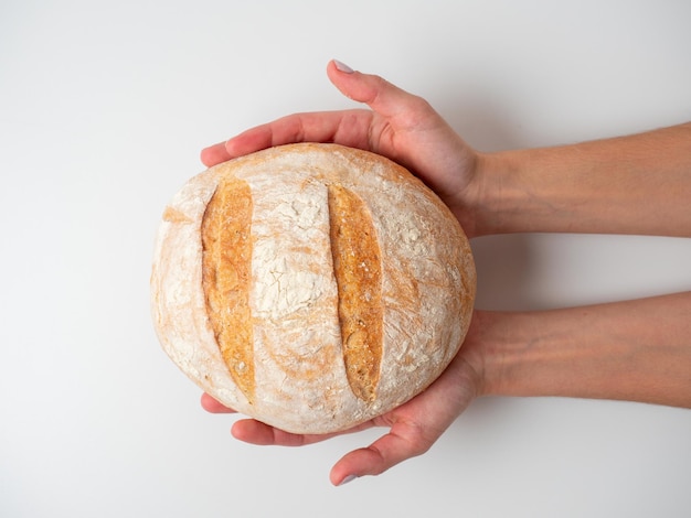 Closeup of hands holding freshly baked round wheat bread with a crispy crust on a white background Top view flat lay