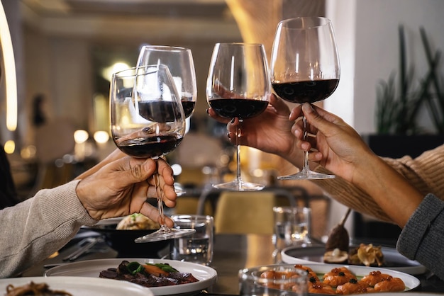 Closeup of hands holding glasses toasting red wine at restaurant - Group of friends celebrate clinking wineglasses