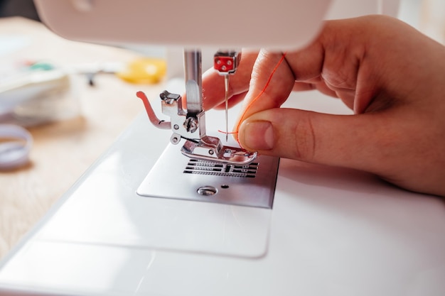 Closeup hands inserting thread into sewing machine needle