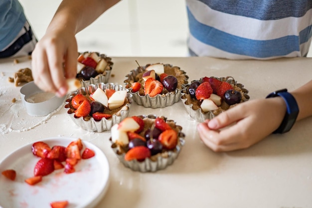 Closeup hands of little boy cooking fresh summer dessert with berry and fruits serving at kitchen