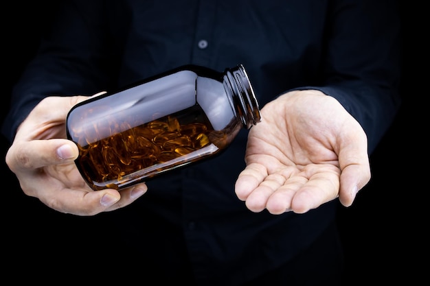 A closeup of the hands of a man holding a jar of fish oil capsules pours capsules on his palm