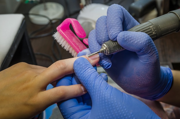 Closeup of the hands of the master  makes a hardware  manicure to the client