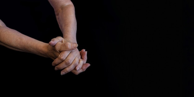 Closeup the hands of an old woman in wrinkles on a black background copy paste