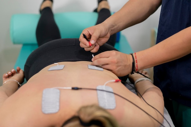 Closeup to the hands of a physiotherapist connecting the electrodes that a patient has on his back