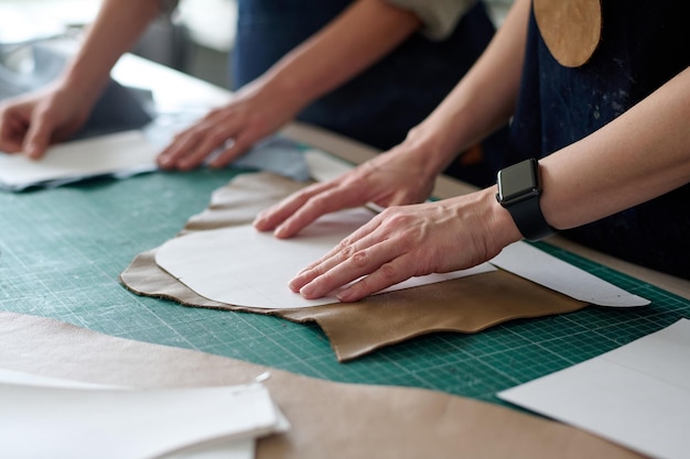 Closeup of hands of two female tailors or tanners with sewing patterns