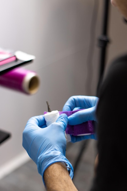 Closeup of the hands of unrecognizable tattoo artist wearing sterile blue gloves while preparing the machine for tattooing in a modern studio