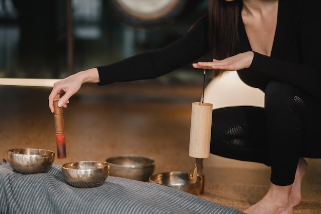 Photo closeup of the hands of a young woman transmitting a message with the help of singing bowls and a koshi bell to another girl sound therapy