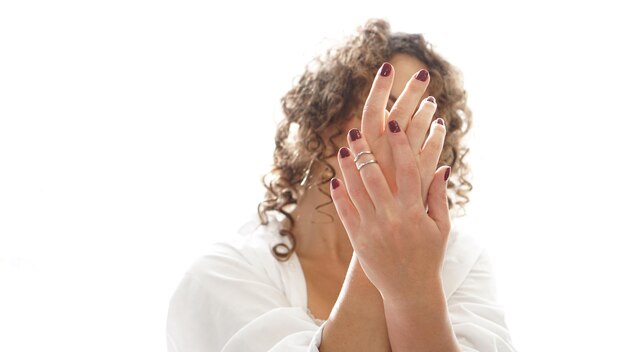 Photo closeup of hands of a young woman with dark red manicure on nails in front of face against white background