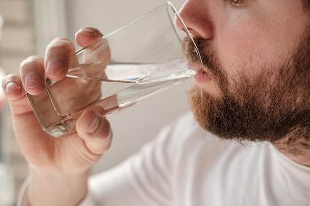 Closeup of a handsome bearded man drinking clear water from a transparent glass