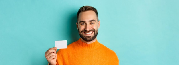 Closeup of handsome caucasian man going on shopping showing credit card and smiling standing over tu