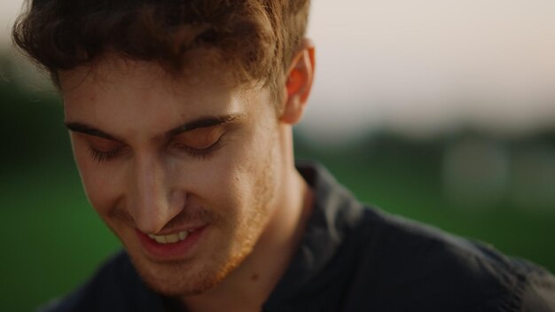 Closeup handsome man flirting with camera outdoors Portrait of sexy model guy looking at camera on meadow at sunset Attractive male person posing at summer park