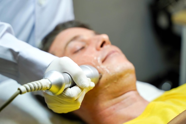 Photo closeup handsome man having therapy to stimulate facial skin and facial ultrasonic skincare treatment by professional cosmetologist wellbeing