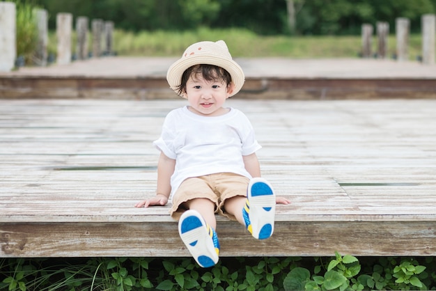 Closeup happy asian kid with smile face sit at wood pathway in the park background