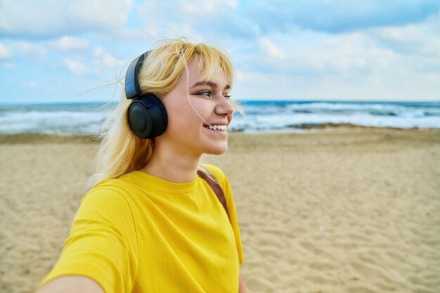 Closeup of happy face of teenage blonde in headphones on the beach copy space