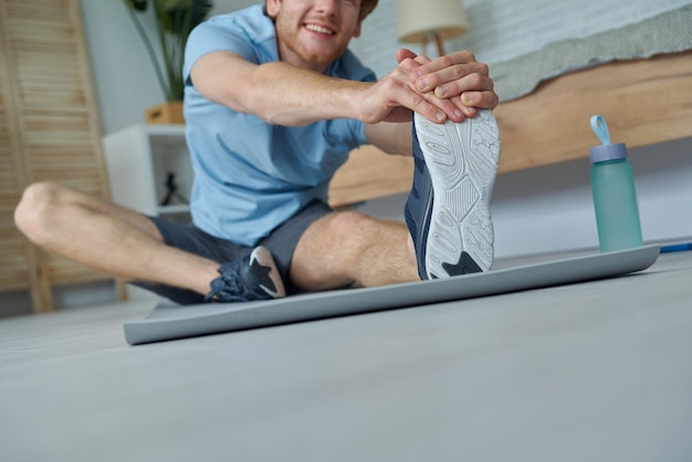 Closeup of happy man in sports clothing doing stretching exercise at home