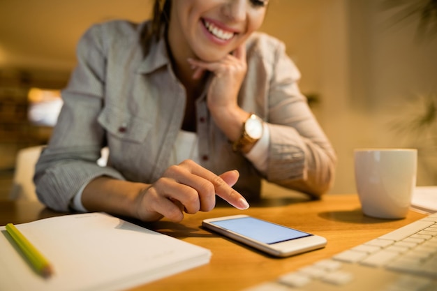 Closeup of happy woman surfing the net on her smart phone in the evening at home