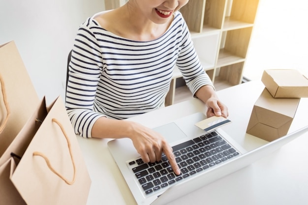 Closeup of happy young woman holding credit card inputting card information while and using laptop computer at home. Online shopping concept.