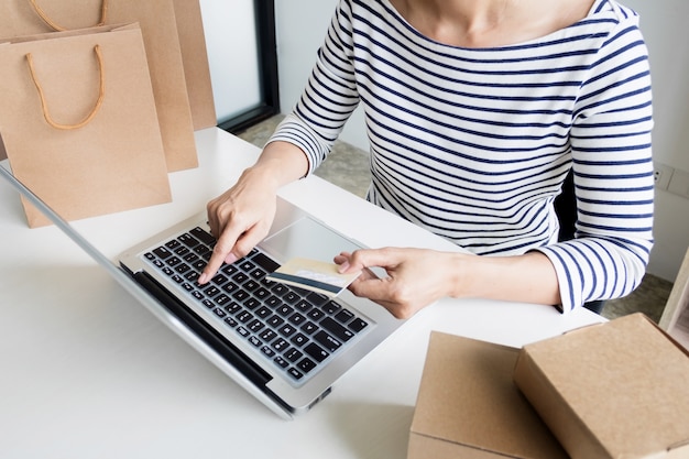 Closeup of happy young woman holding credit card inputting card information while and using laptop computer at home. Online shopping concept.