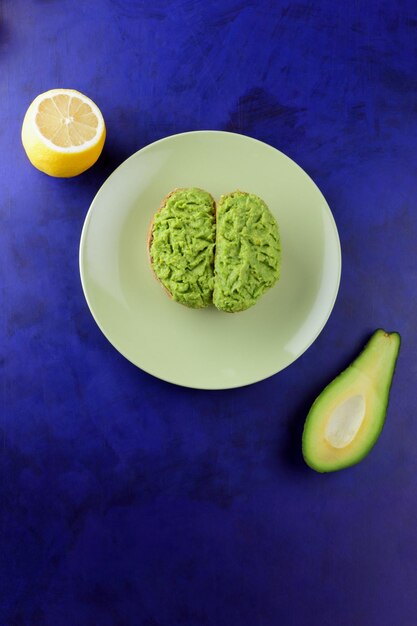 Closeup of a healthy snack food on a blue background Two vegetarian toasts with avocado and lemon on a green plate View from above