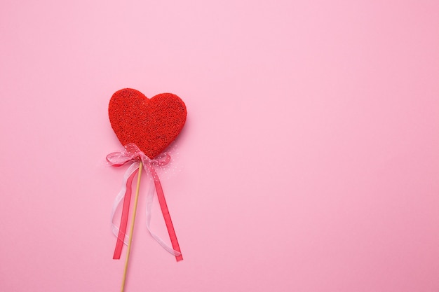 Closeup of a heart with a decor on a stick on a pink isolated background. Spell love in white letters.