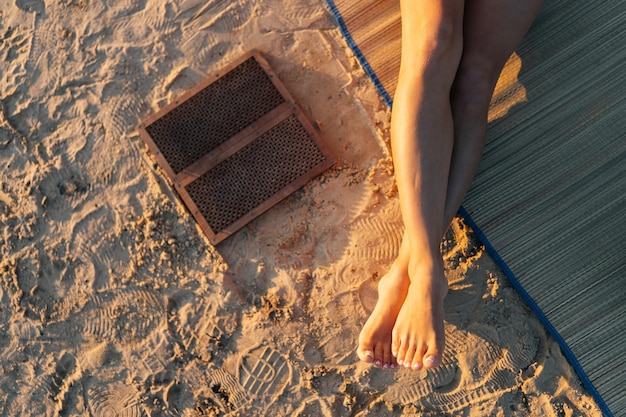 Closeup highangle view of of unrecognizable woman sitting on yoga mat with Sadhu board on sandy beach at summer sunny morning