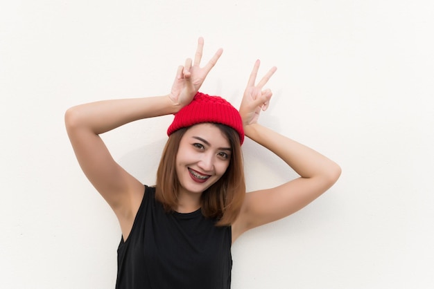 Photo closeup hipster girl wear red hat show two fingers on your headshe has beautiful smilecute asian womanlifestyle of hip girl