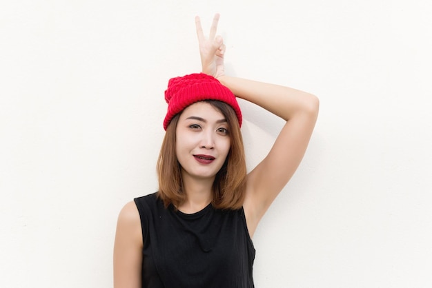 Closeup hipster girl wear red hat show two fingers on your headshe has beautiful smilecute asian womanlifestyle of hip girl