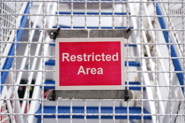 Photo closeup horizontal frame of a red restricted area sign attached to a white netted fence no people