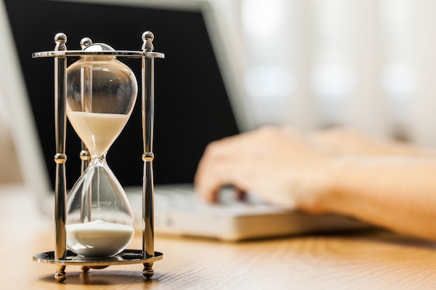 Closeup of a Hourglass with a Person Typing on a Laptop on Background