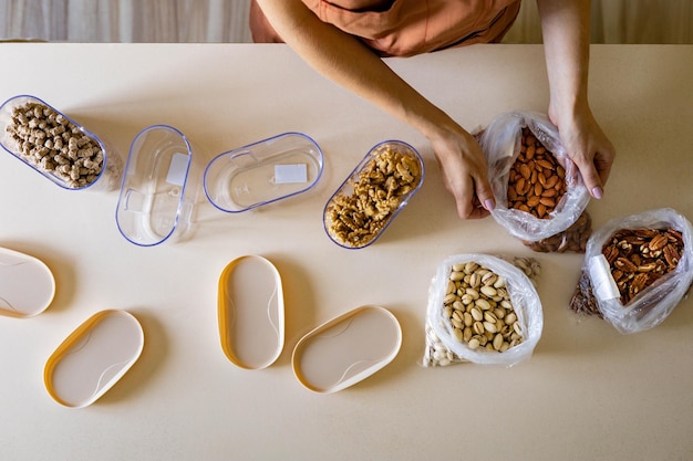 Closeup housewife hands placing nuts plastic package into container box on wooden table at kitchen