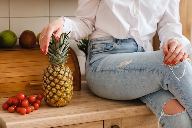 A closeup of a housewife in a white shirt and jeans is sitting on a table and fruits and vegetables are lying nearby The concept of healthy eating