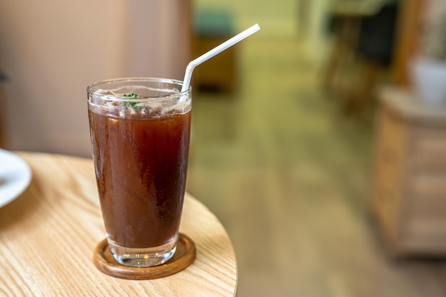 Closeup of Iced Black americano in a glass cup mug on wood desk office desk in coffee shop at the cafe in gardenduring business work concept