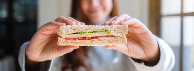 Closeup image of an asian woman holding and eating whole wheat sandwich