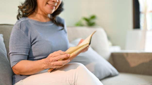 Closeup image an Asianaged woman reading a book on sofa in her living room