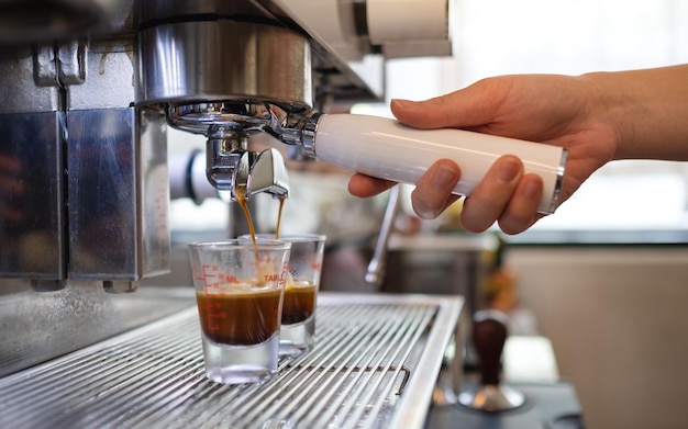 Closeup image of barista making coffee from coffee machine and pouring into shot glasses