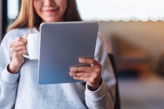 Closeup image of a beautiful young asian woman holding and using digital tablet while drinking coffee