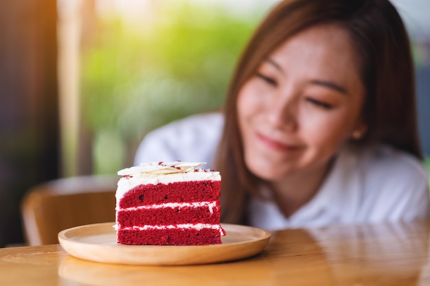 Closeup image of a beautiful young asian woman looking at a piece of red velvet cake in wooden tray on the table