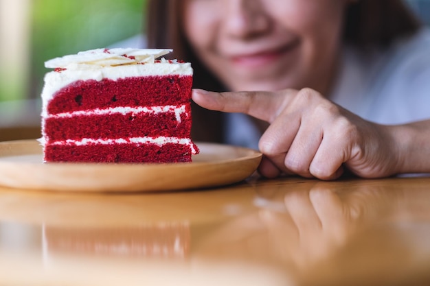 Closeup image of a beautiful young asian woman looking and touching a piece of red velvet cake in wooden tray on the table