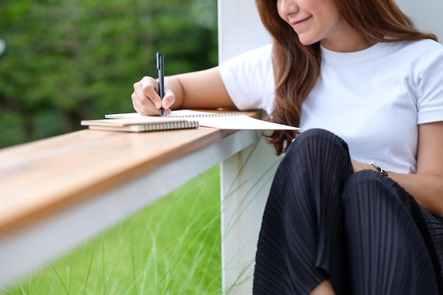 Closeup image of a beautiful young asian woman writing on a notebook in the outdoors