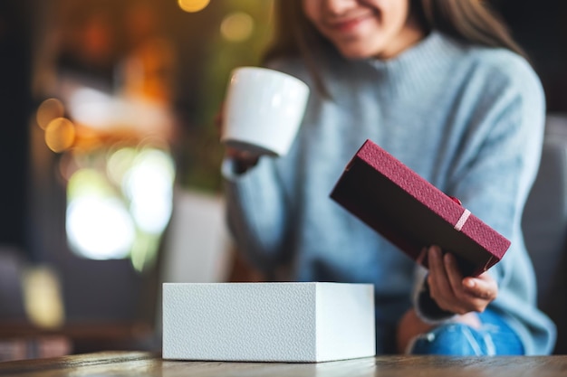 Closeup image of a beautiful young woman opening a gift box while drinking coffee