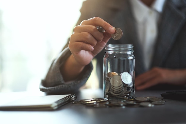 Closeup image of a businesswoman collecting and putting coins in a glass jar for saving money concept