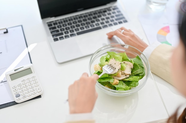 Closeup image of a busy Asian businesswoman having lunch at her desk