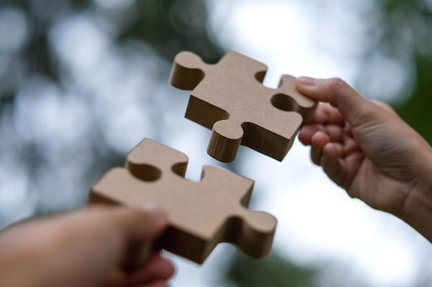 Closeup image of a couple people holding and putting a piece of wooden jigsaw puzzle together